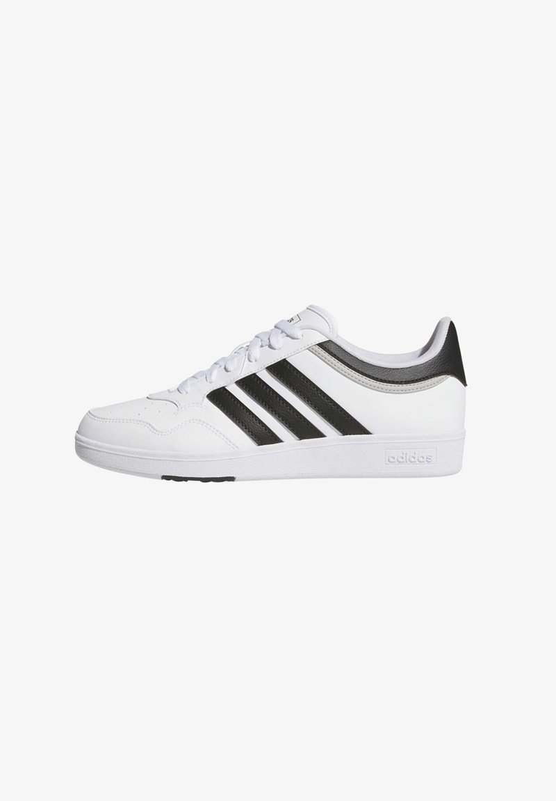 White sneakers with three black stripes, textured material, padded tongue, and a black heel accent. Rubber sole and lace-up design.