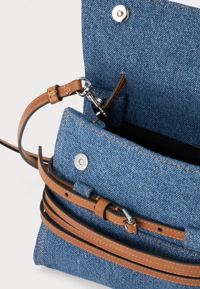 Μπλε τζιν τσάντα crossbody με καφέ ρυθμιζόμενο δερμάτινο λουρί και ασημένιο μαγνητικό κούμπωμα, εμφανιζόμενη ανοιχτή με ορατή εσωτερική επένδυση.