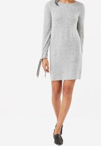Vestido gris de manga larga hecho de una tela suave, con cuello redondo y detalles de lazo en los puños. El diseño es recto y llega a la rodilla.