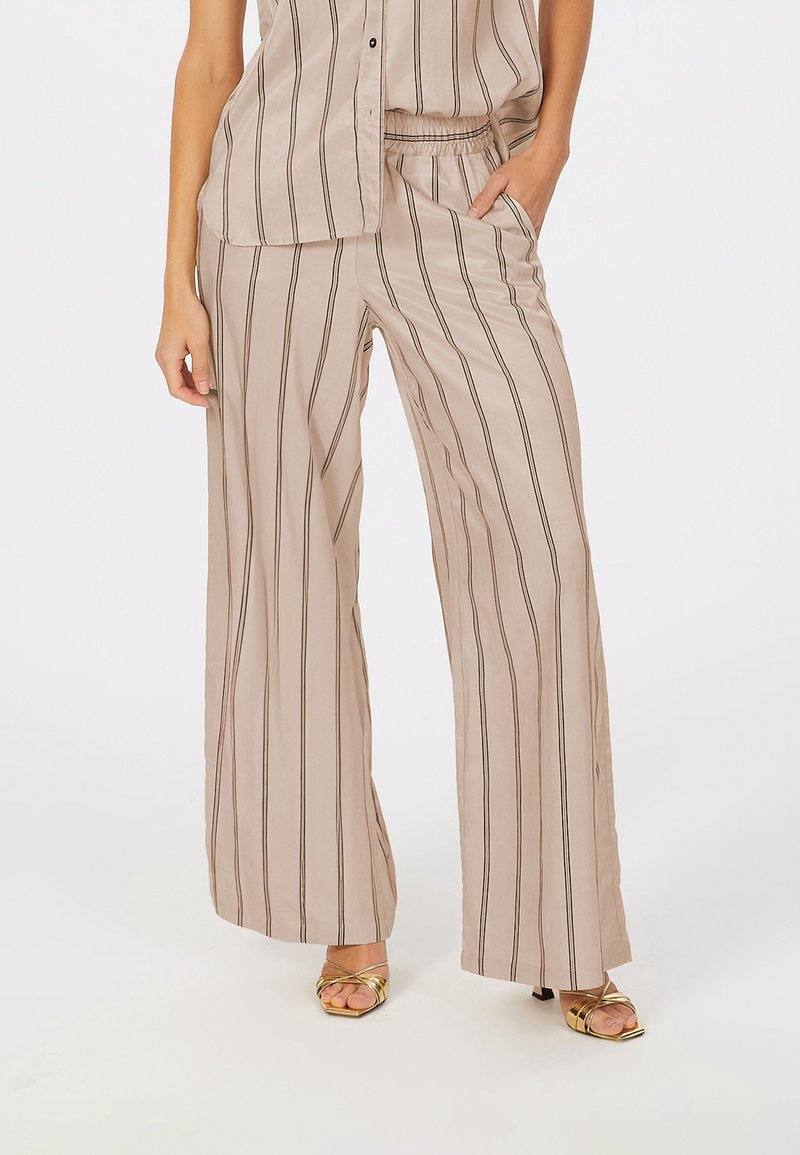 Beige gestreifte, weit geschnittene Hose mit elastischem Bund, kombiniert mit einem passenden, legeren Oberteil. Der Stoff wirkt glatt und leicht.