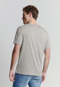 Grijze T-shirt met korte mouwen, gemaakt van zachte stof en met een ronde hals. De achterkant heeft een gladde textuur en een eenvoudig ontwerp zonder versieringen.