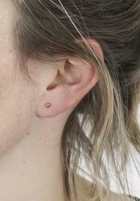 Kleine, runde, roségoldene Ohrstecker auf einem hellen Hautton, positioniert im Ohrläppchen, mit einer glatten metallischen Textur und minimalistischen Design.