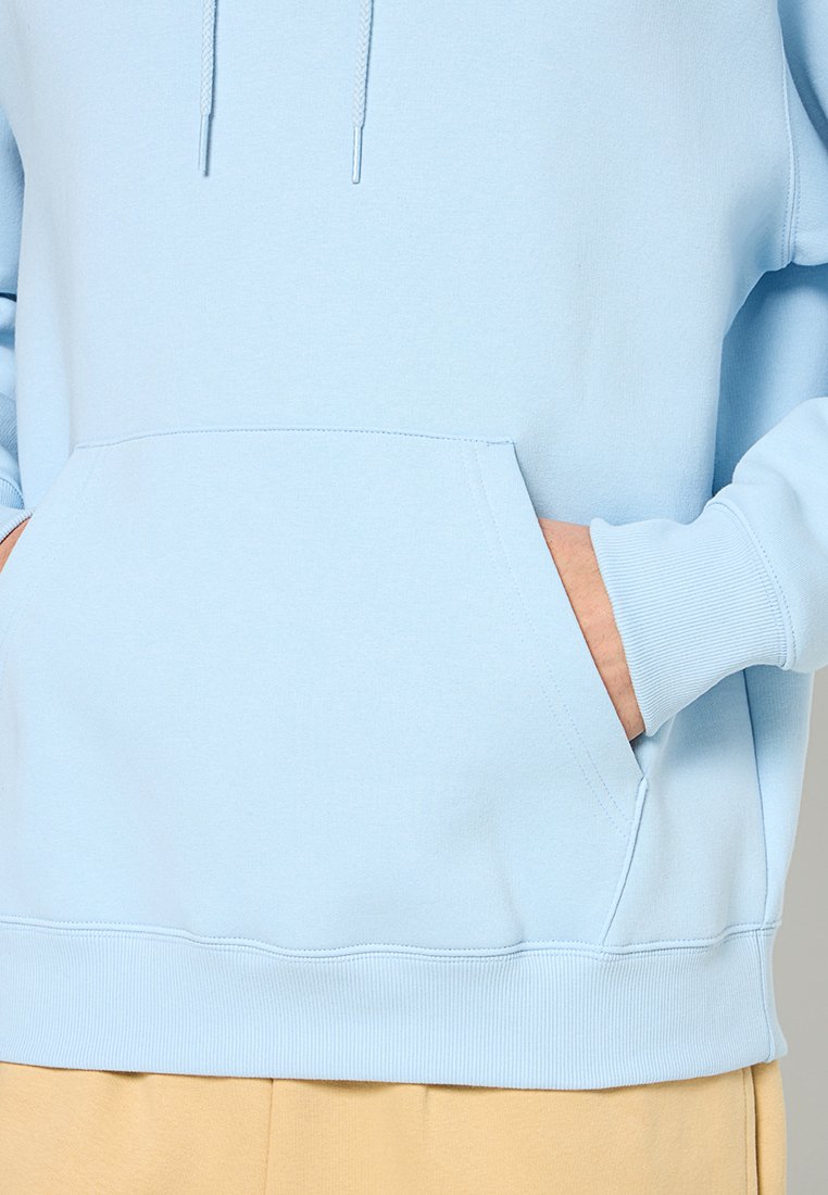Hoodie bleu clair en tissu doux, doté d'une poche avant, de bords côtelés et d'une capuche avec cordon de serrage, offrant une coupe décontractée.