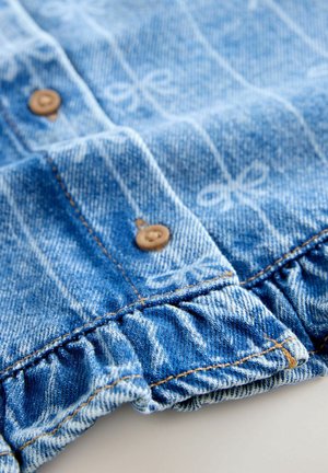 Jeansplagg med ljusblå färg och ett subtilt rosettmönster. Den har knappstängning och en volangkant vid nederkanten.