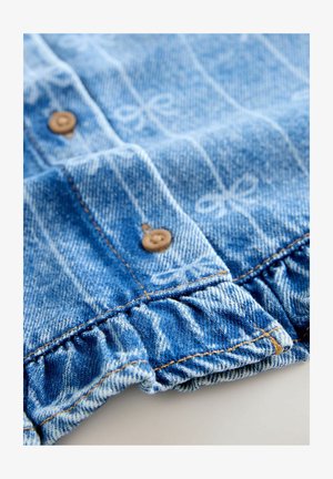 Traperi odjeća svijetloplave boje s diskretnim uzorkom mašni. Ima kopčanje na gumbe i detalj naboranog ruba.