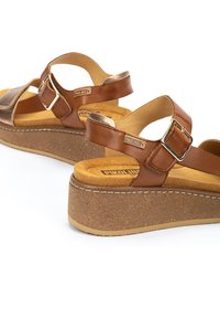 Sandalias de plataforma de cuero marrón con tira ajustable y hebilla de metal, plantilla acolchada y suela de corcho texturizada.