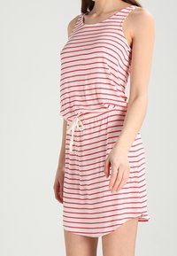 Raidallinen mekko, jossa on punaisia ja valkoisia vaakaosuuksia. Pehmeää kangasta, olkaimeton malli, rento istuvuus ja nyöritettävä vyötärö. Suora helma.