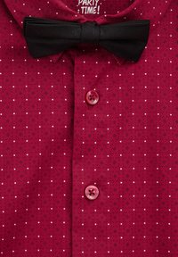 Röd skjorta med vita prickar, kort krage och svart fluga. Har rosa knappar, strukturerad tyg och etikett med texten "PARTY TIME!" inuti kragen.