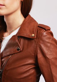 Brown leather jacket with a notched collar, zippered front, and metallic buttons. Smooth texture and fitted design highlight the craftsmanship.