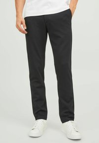 Black, fitted trousers made of smooth fabric, featuring pockets and a flat front design, paired with white sneakers.