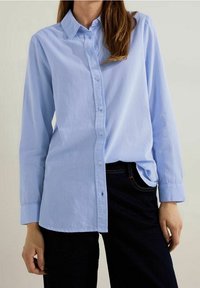 Ljust blå, långärmad skjorta med knappstängning och klassisk krage samt subtila vertikala ränder, kombinerad med mörka jeans. Strukturerad tyg.