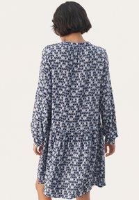 Abito a maniche lunghe in blu e bianco con motivo geometrico, realizzato in tessuto leggero, con scollo arricciato e orlo a balze.