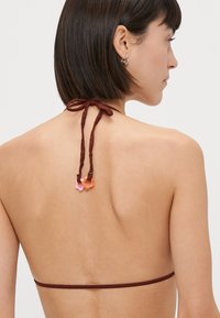 Bruin bikini-top met dunne bandjes die om de nek zijn geknoopt, voorzien van kleurrijke bloemenvormige hardware in roze en oranje aan de achterkant.
