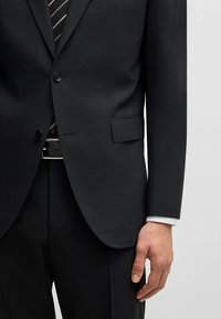 Jacket da completo grigio scuro con una finitura tessurizzata, chiusura a un bottone e due tasche frontali, abbinato a una cravatta a righe e una cintura nera.