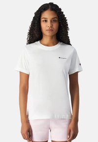 Hvid bomulds t-shirt med korte ærmer, rund halsudskæring og et lille rødt broderet logo på venstre bryst og ærme.