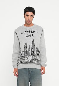 Grijze gebreide trui met een zwarte grafiek van de Londense skyline en de tekst "CENTRAL LDN." op de voorkant. Ronde hals en lange mouwen.
