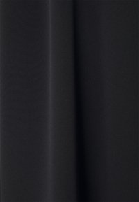 Tissu noir avec une surface lisse légèrement texturée, drapé pour créer des plis verticaux et des ombres douces.
