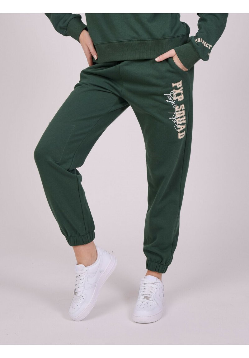 Groene sweatpants met taps toelopende boorden, featuring een 'PYP SQUAD' print in crèmekleur. Gecombineerd met witte sneakers voor een casual look.