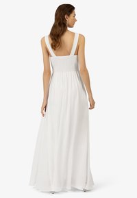 Weißes Maxikleid mit gerafftem Oberteil, breiten Trägern und einem fließenden Rockdesign. Glatte Textur mit leichtem Glanz. Rückansicht sichtbar.