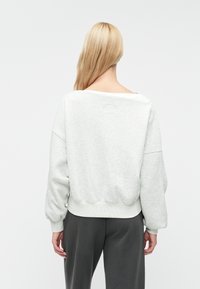 Svijetlosivi dukserica s širokim izrezom, spuštenim ramenima i rebrastim manžetama. Mekani, teksturirani materijal izgleda ležerno i opušteno.