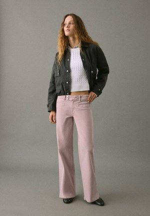 Chaqueta negra corta con bolsillos frontales, suéter blanco texturizado, pantalones de pierna ancha rosa claro y zapatos negros con acentos.
