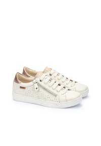 Zapatillas de cuero blancas con diseño perforado, acentos en marrón claro contrastantes, punta redonda, suela plana de goma y detalle de cremallera lateral.