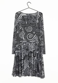 Vestido de manga larga en blanco y negro con un patrón floral en espiral, cuerpo ajustado y falda acampanada con pliegues. Cuélga de un gancho negro.