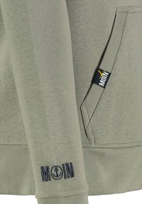 Groene katoenen hoodie met ribgebreide manchetten, met een marineblauw "MOIN" logo en ankerborduursel op de mouw en een ontwerp van zijzakken.