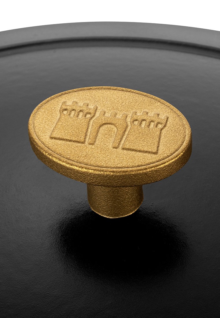Goldfarbener Gusseisenknopf mit einem Burgdesign, strukturiertem Finish und kreisförmiger Form, montiert auf einer schwarzen Gusseisenoberfläche.