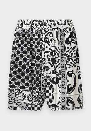 Pantaloncini a motivo bianco e nero con design patchwork, inclusi quadrati a scacchiera, forme astratte e testo "Carlo Colucci" su righe verticali.