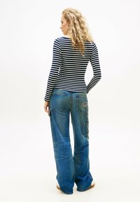 Marineblau-weiß gestreiftes Langarmoberteil, tailliert, kombiniert mit lockeren blauen Denim-Hosen mit großen Taschen und einem used-Look.