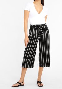 Culottes à rayures noir et blanc avec un détail de taille à nouer, présentant un design à jambes larges et un tissu lisse. Associés à un haut blanc ajusté.