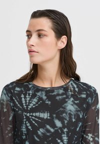 Langärmliges Oberteil aus dunklem Stoff mit einem Batikmuster in Blau- und Schwarztönen. Rundhalsausschnitt, durchsichtige Ärmel und strukturierter Körper.