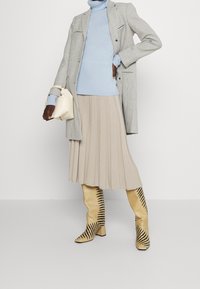 Beige plisserad kjol, ljusblå turtleneck, rutigt kavaj och gula stövlar med svarta ränder. Accenterad med en krämfärgad handväska.