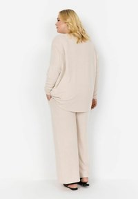 Maglia di maglia beige chiaro con maniche a sbuffo, abbinata a pantaloni larghi coordinati. Tessuto morbido, vestibilità rilassata e tasche laterali sui pantaloni.