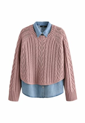 Różowy sweter dzianinowy z teksturowanym wzorem w warkocz i długimi rękawami, założony na jasnoniebieską koszulę dżinsową z wyrazistym kołnierzykiem i zapięciem na guziki.