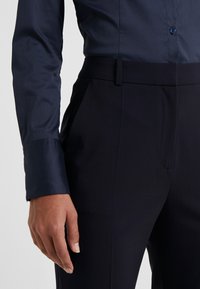 Chemise bleu marine à boutons avec une texture lisse associée à un pantalon sombre sur mesure avec poches et un design à plat.