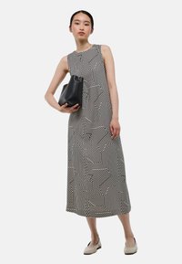 Robe sans manches à motif géométrique noir et blanc, de longueur mi-cuisse, associée à un sac à main noir et des ballerines claires.