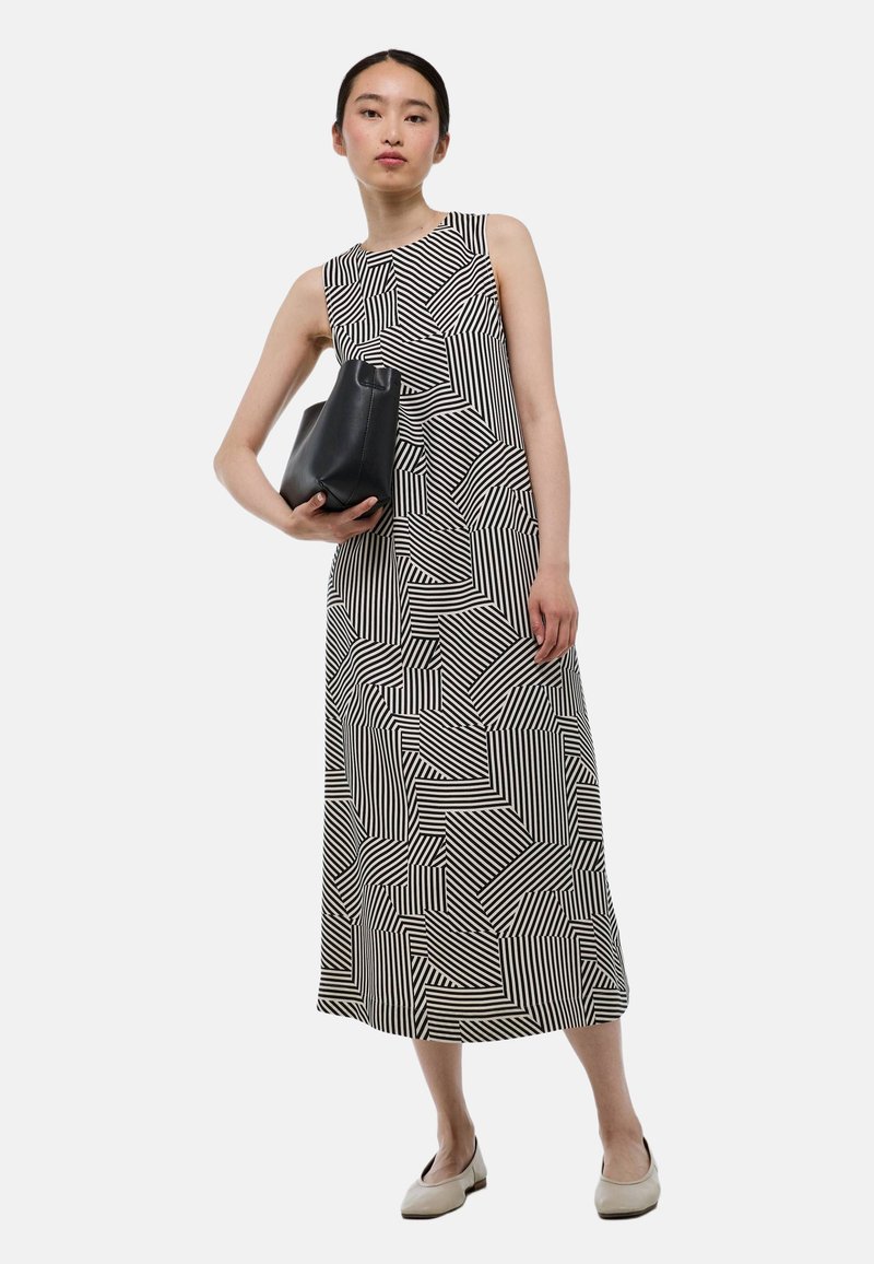 Robe sans manches à motif géométrique noir et blanc, de longueur mi-cuisse, associée à un sac à main noir et des ballerines claires.