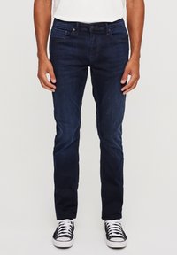 Tamno plave traperice s pet džepova, ravnog kroja, s blagim rastezanjem, završene detaljima crno-bijelih tenisica.