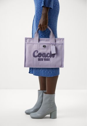 Lawendowa torba typu tote z tkaniny z haftowanym logo "Coach New York", dwoma uchwytami i odpinaną metką, w zestawie z szarymi botkami za kostkę.