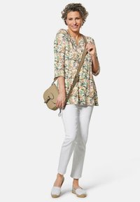 Bloemen tuniektop met driekwart mouwen, gecombineerd met witte slim-fit broeken en lichte espadrilles. Draagt een kleine beige schoudertas.