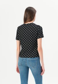 Black short-sleeve shirt with white polka dots, featuring a round neck and textured fabric. Paired with blue denim jeans.