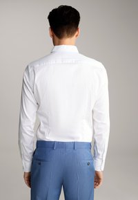 Weißes Langarmhemd mit glatter Textur, getragen mit hellblauen, taillierten Hosen mit geknöpften Gesäßtaschen.