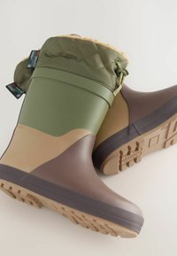 Grüne und braune wasserdichte Stiefel mit einem gesteppten grünen Obermaterial, hellbraunen Akzenten und strukturierten Gummisohlen in einem klobigen Design.