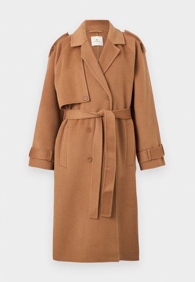 Lungo cappotto marrone in lana di cammello con ampi rever, bottoni doppiopetto, spalline, vita con cintura e cinturini ai polsi.