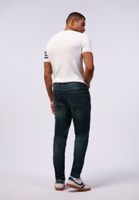Camisa de manga corta blanca con rayas negras en las mangas, combinada con jeans ajustados oscuros y zapatillas blancas con detalles en azul.