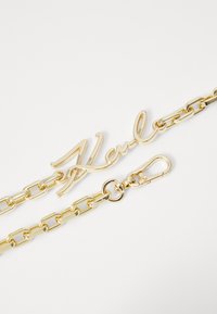 Collana d'oro con un nome 'Karl' in corsivo, texture liscia, dotata di gancio e maglie intrecciate. Ideale per accessori o decorazioni.