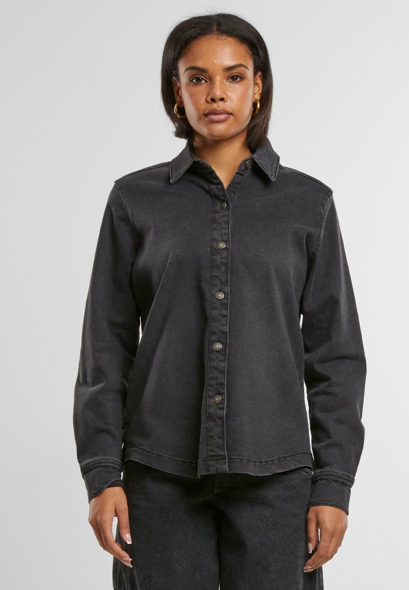 Zwarte spijkerblouse met lange mouwen, knoopsluiting aan de voorkant, puntige kraag en licht toelopende zoom. Heeft zichtbare stiksels en een geborstelde textuur.