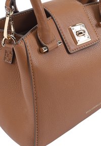 Sac à main en cuir marron avec un design structuré, quincaillerie dorée et accents cousus. Il dispose de poignées supérieures et d'un logo visible sur le côté.